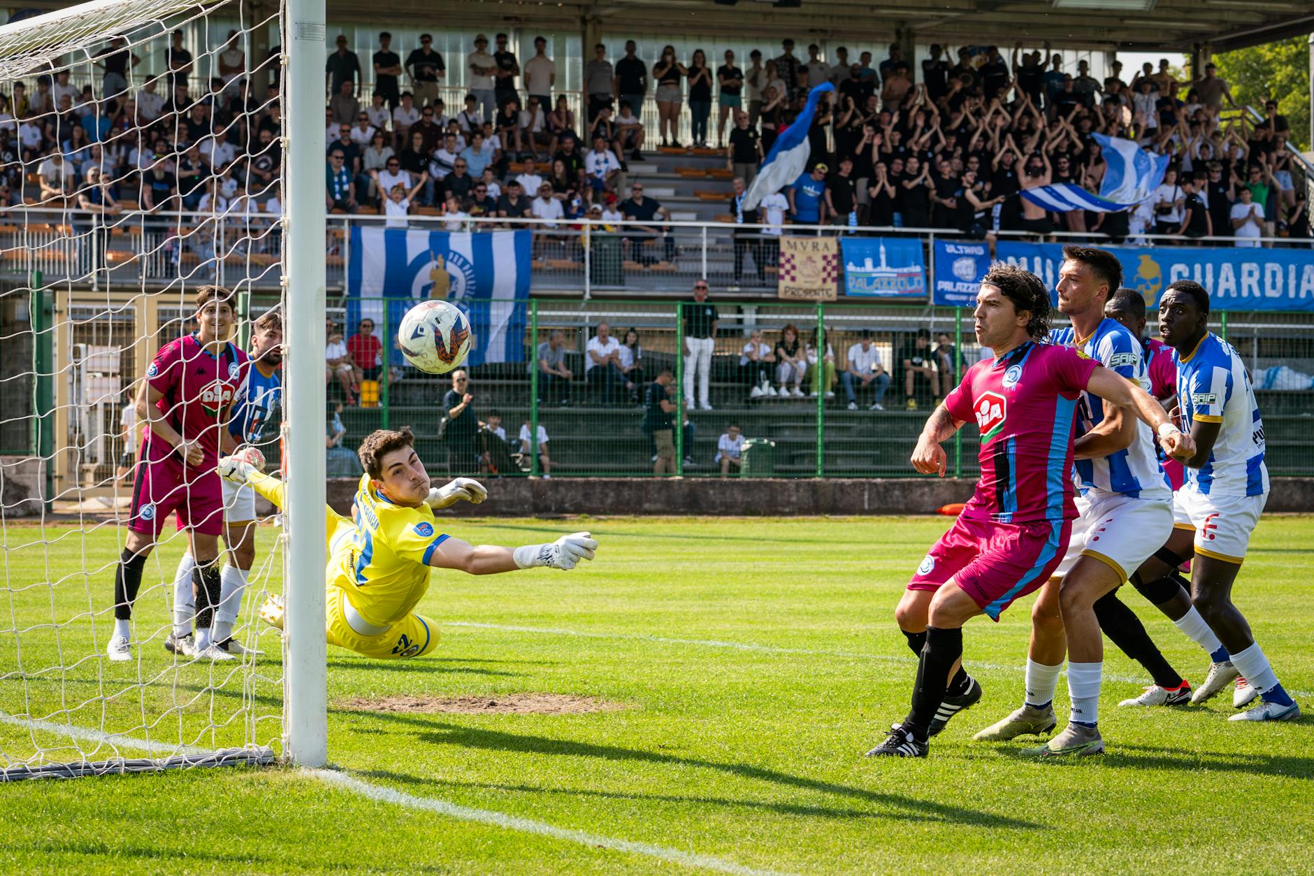 Intense soccer game moment as goalkeeper attempts a save in a crowded stadium.